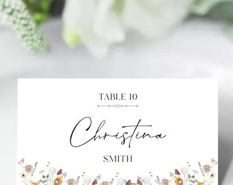 May include: White wedding table card with a floral border. The card says "Table 10" and "Christina Smith" in black text.