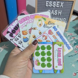 May include: A selection of illustrated cards with vibrant designs and text. The cards showcase pandas, bees, mushrooms, and teacups. Text includes "Panda Pou", "Let's Get Par-Tea", "Bee Kind", and "So Mushroom".