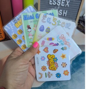 May include: A selection of spring and Easter-themed stickers. Designs include bees, Easter eggs, flowers, and the words "Spring" and "Easter". The stickers are in clear plastic sleeves.