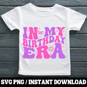 Puede incluir: Una camiseta blanca con un dise&ntilde;o rosa y morado que dice "In My Birthday Era". El dise&ntilde;o incluye mariposas, estrellas y flores.