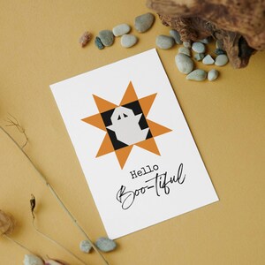 Puede incluir: Una tarjeta blanca con un diseño de Halloween. Presenta un patrón geométrico de estrella en naranja y negro, con un fantasma blanco en el centro. Las palabras "Hello Boo-tiful" están escritas en guión negro.