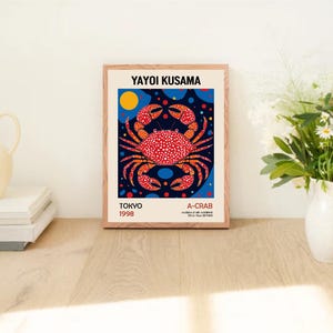 May include: A framed print of a red and white crab with black polka dots on a blue background with white polka dots. The print is titled "A-Crab" and includes the artist's name "Yayoi Kusama" and the date "Tokyo 1998".