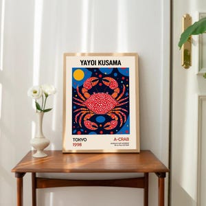 May include: A framed poster with a colorful illustration of a crab on a blue background with white and orange polka dots. The poster is titled "A-CRAB" and includes the artist's name "YAYOI KUSAMA" and the date "TOKYO 1998".