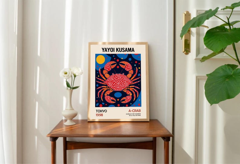 May include: A framed poster with a colorful illustration of a crab on a blue background with white and orange polka dots. The poster is titled "A-CRAB" and includes the artist's name "YAYOI KUSAMA" and the date "TOKYO 1998".