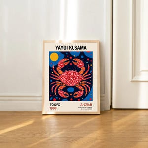 May include: A framed poster with a colorful illustration of a red crab on a blue background with yellow and blue polka dots. The poster has the text "Yayoi Kusama" at the top, "Tokyo 1998" at the bottom left, and "A-Crab" at the bottom right.