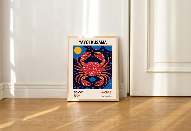 May include: A framed poster with a colorful illustration of a red crab on a blue background with yellow and blue polka dots. The poster has the text "Yayoi Kusama" at the top, "Tokyo 1998" at the bottom left, and "A-Crab" at the bottom right.