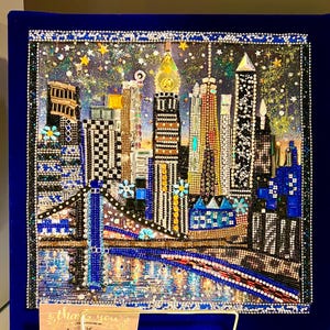 Puede incluir: Una detallada y brillante obra de arte de un paisaje urbano con un puente y rascacielos, creada con varios adornos. La obra de arte está sobre un fondo de terciopelo azul oscuro. Una pequeña tarjeta dice "gracias por apoyar mi pequeña empresa".