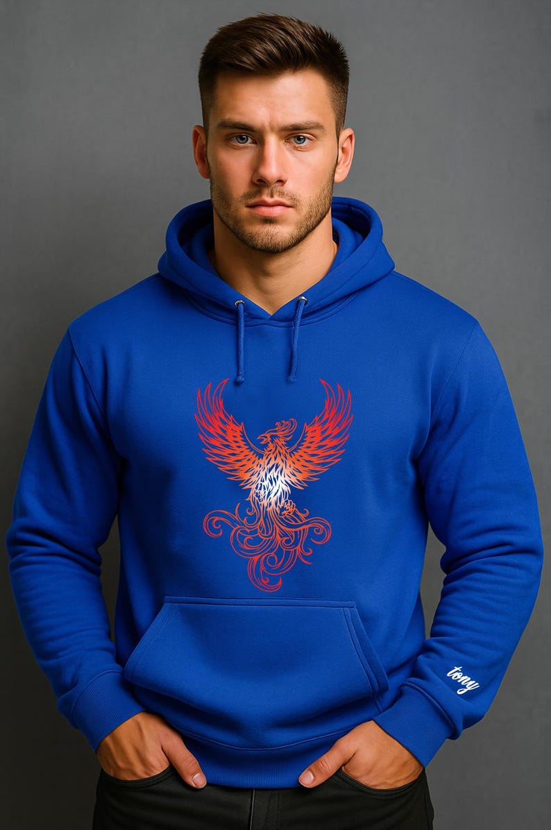 A man stands confidently against a solid gray background wearing a royal blue hoodie. The front of the hoodie features a bold red and orange phoenix graphic with intricate, flame-like detailing. On the right sleeve cuff, the name "tony" is embroidered in a small, white cursive font. The model has short dark hair, a trimmed beard, and a serious expression, with his hands tucked into the front pocket of the hoodie.