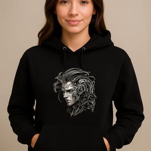 May include: Black hooded sweatshirt featuring a detailed silver and white graphic of a stylized face with intricate mechanical elements. The design is on the front of the sweatshirt, which has a kangaroo pocket.