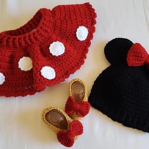 May include: A red crocheted skirt with white polka dots, a black crocheted hat with red bow, and two pairs of yellow crocheted shoes with red bows. The set is designed for a baby or toddler.