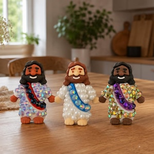 May include: Three small figurines of figures with long hair and beards, each wearing a white robe with a diagonal sash. The first has a dark blue sash, the second a light blue sash, and the third a purple sash, all covered in iridescent rhinestones.