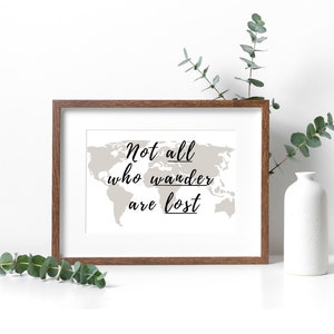 Può includere: Una stampa incorniciata con uno sfondo di mappa del mondo e il testo "Not all who wander are lost". La cornice è in legno marrone.