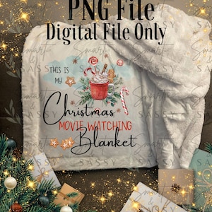 May include: A white faux fur blanket with a Christmas-themed design. The design features a mug of hot chocolate with whipped cream, candy canes, gingerbread cookies, and a Christmas tree. The text "This is my Christmas Movie Watching Blanket" is written in black lettering.