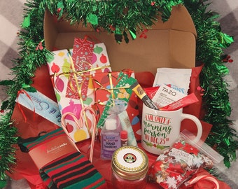 May include: A Christmas gift box containing wrapped presents, candy canes, socks, a mug, and other festive items. The mug says "I AM ONLY A morning person ON DEC.25th". The box is decorated with green garland and red tissue paper.