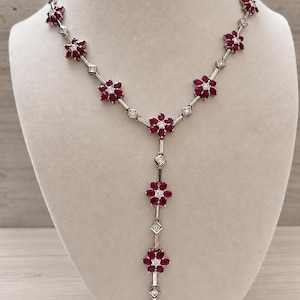 Puede incluir: Un collar en forma de Y que presenta una serie de eslabones de metal plateado conectados por motivos en forma de flor. Cada flor está compuesta por seis rubíes de color rojo intenso en talla marquesa alrededor de un diamante blanco.