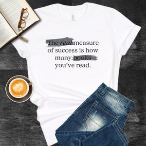 May include: White t-shirt with the text "The real measure of success is how many books you've read." printed in black with gray brushstrokes underneath each line.