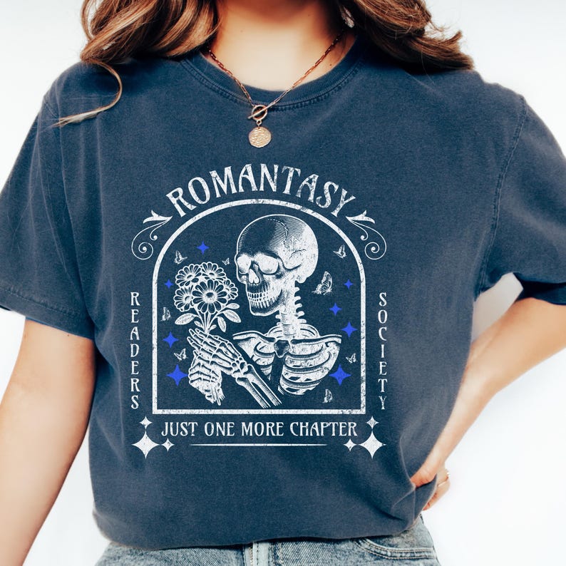 May include: A navy blue t-shirt with a vintage-style graphic of a skeleton holding flowers. The graphic includes the text "Romantasy Readers Society" and "Just One More Chapter".