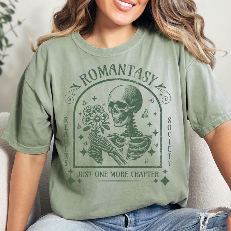 May include: Green t-shirt with a vintage-style graphic of a skeleton holding flowers. The graphic says "Romantasy Readers Society" and "Just One More Chapter".