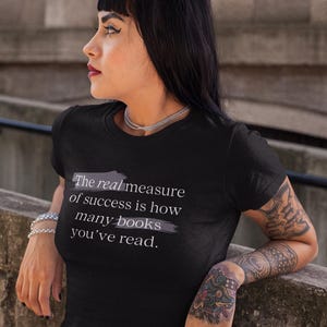 May include: A black t-shirt with a white graphic that reads "The real measure of success is how many books you've read."