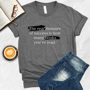 May include: Gray t-shirt with the text "The real measure of success is how many books you've read." printed in black with a black brushstroke effect.
