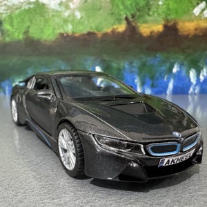 May include: A dark gray model car with silver wheels and blue accents. The car has a sleek, modern design with a low profile and a prominent front grille. The license plate reads "AKHEEL".