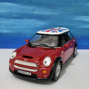 Könnte beinhalten: Rotes Mini Cooper Spielzeugauto mit einer Union Jack Flagge auf dem Dach. Das Auto hat ein schwarzes Nummernschild mit der Aufschrift "ERICA".