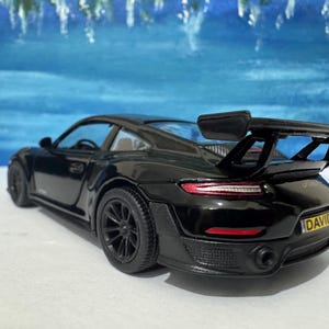 以下が含まれることがあります： 黒いポルシェ911 GT2 RSの玩具カーモデル。大きなリアスポイラーと「DAVID」と書かれた黄色のナンバープレートが付いています。