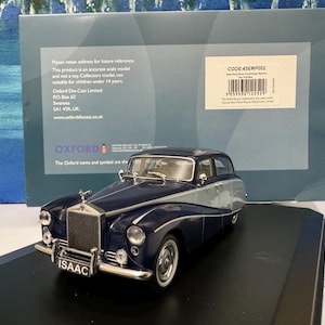 May include: A dark blue and silver 1950s Rolls Royce Silver Wraith diecast model car. The car is on a black display base. The car has the word "ISAAC" on the number plate.