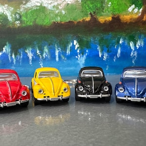 Puede incluir: Cuatro coches de juguete en miniatura rojos, amarillos, negros y azules. Los coches están alineados, cada uno con un color y diseño distintos. El fondo presenta una pintura de un paisaje con agua y árboles.