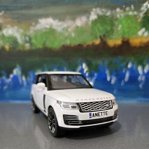 May include: A white Range Rover model car with black wheels and trim. The front of the car has a black grill and the license plate reads "ANETTE". The word "RANGE ROVER" is above the grill.