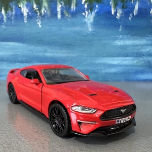 Könnte beinhalten: Ein rotes Spielzeugauto mit schwarzen Rädern. Das Auto hat ein schlankes Design mit schwarzem Innenraum und einem Frontgrill mit dem Text "ERIN". Der Hintergrund ist eine blau-weiß gemalte Szene.