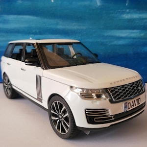 Puede incluir: Un modelo de coche Range Rover blanco con ruedas y molduras negras. El modelo tiene una parrilla negra y la palabra "RANGE ROVER" está encima de la parrilla. La matrícula dice "DAVID".