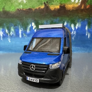 May include: A blue toy van with a black front bumper and a roof rack. The van has the word "DAVID" on the license plate. The van is a miniature model.