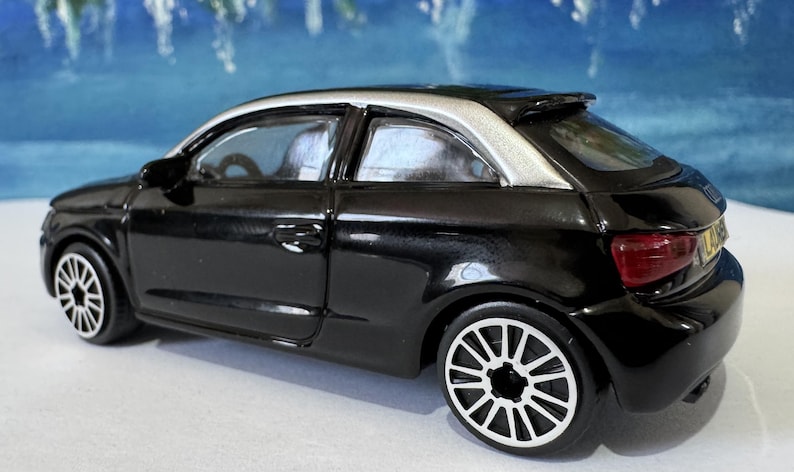 Peut inclure: Une petite voiture noire avec un toit argent&eacute; et des jantes blanches. Le v&eacute;hicule miniature a un aileron et des feux arri&egrave;re rouges. C'est un mod&egrave;le r&eacute;duit, probablement un jouet ou un objet de collection.