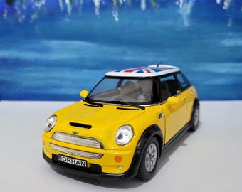 Puede incluir: Un coche de juguete amarillo modelo Mini Cooper con una bandera del Reino Unido en el techo. El coche tiene detalles negros y una matrícula negra que dice "ORHAN".