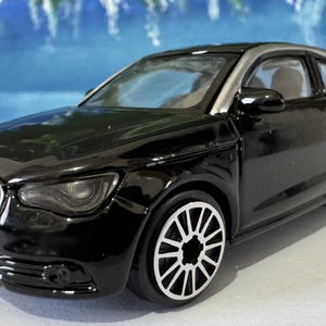 Peut inclure: Une voiture jouet noire avec des accents argent&eacute;s, avec une plaque d'immatriculation "LAUREN". La voiture a des roues d&eacute;taill&eacute;es et un design &eacute;pur&eacute;, ressemblant &agrave; une petite voiture de sport. Le fond est bleu flou.