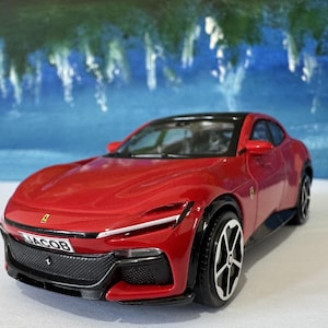 May include: A red toy car with a black roof and black wheels. The car has a license plate that reads "JACOB". The car is a miniature model of a sports car.