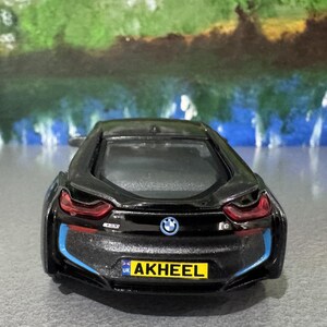 May include: A black BMW i8 toy car with blue and red accents. The car has a license plate that reads "AKHEEL". The BMW logo is visible on the rear of the car. The car is a miniature model.