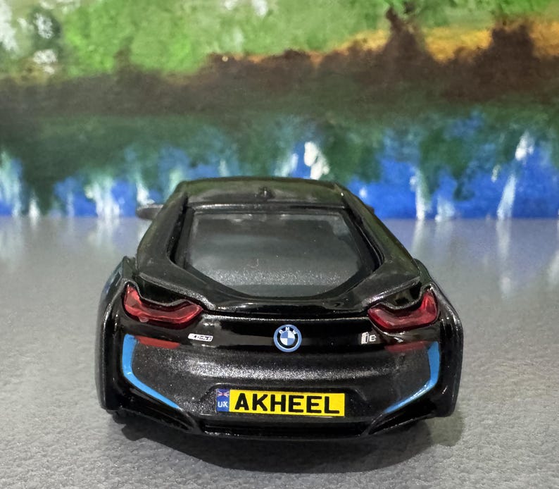 May include: A black BMW i8 toy car with blue and red accents. The car has a license plate that reads "AKHEEL". The BMW logo is visible on the rear of the car. The car is a miniature model.