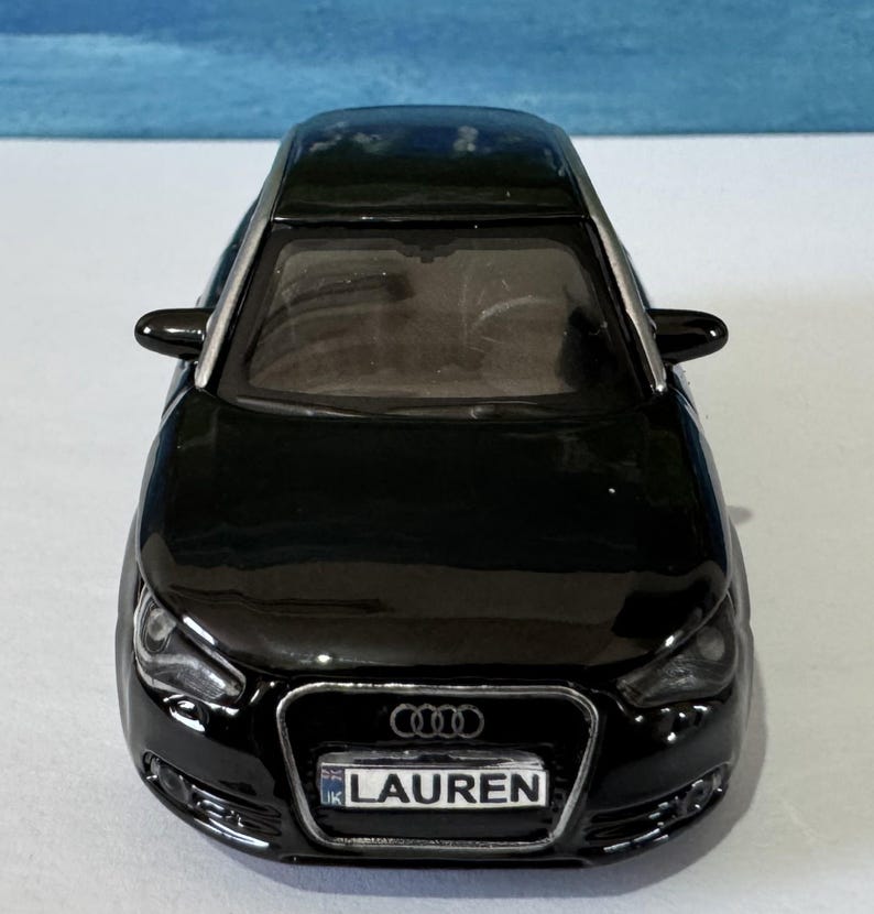 Peut inclure: Une voiture jouet noire avec le nom "LAUREN" sur la plaque d'immatriculation. La voiture a une finition brillante, des d&eacute;tails argent&eacute;s et le logo Audi &agrave; l'avant. C'est une maquette d'une voiture moderne.