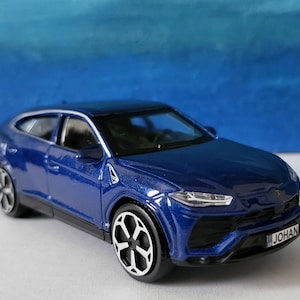 May include: A blue toy car model of a Lamborghini Urus with black wheels and a license plate that reads "JOHAN".