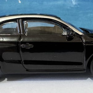 Peut inclure: Une voiture jouet noire avec un toit blanc et des roues argent&eacute;es. La voiture a un design &eacute;l&eacute;gant avec des phares et des feux arri&egrave;re d&eacute;taill&eacute;s. Les roues ont un motif unique.