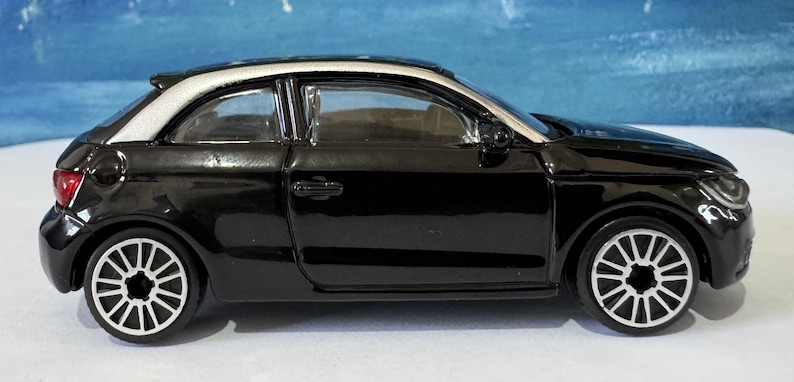 Peut inclure: Une voiture jouet noire avec un toit blanc et des roues argent&eacute;es. La voiture a un design &eacute;l&eacute;gant avec des phares et des feux arri&egrave;re d&eacute;taill&eacute;s. Les roues ont un motif unique.