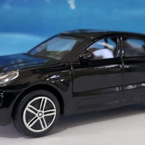 May include: Black toy car model of a Porsche Macan SUV. The car has a detailed exterior with black paint and silver wheels.