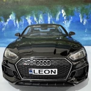 Könnte beinhalten: Ein glänzend schwarzes Audi RS5 Modellauto. Die Front zeigt einen schwarzen Wabenkühlergrill, das Audi-Logo und ein britisches Nummernschild mit der Aufschrift "LEON".