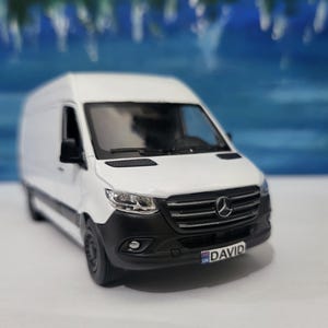 Peut inclure: Camionnette jouet blanche avec une calandre et des phares noirs. La camionnette a un pare-chocs noir et une plaque d'immatriculation qui indique "UK DAVID".