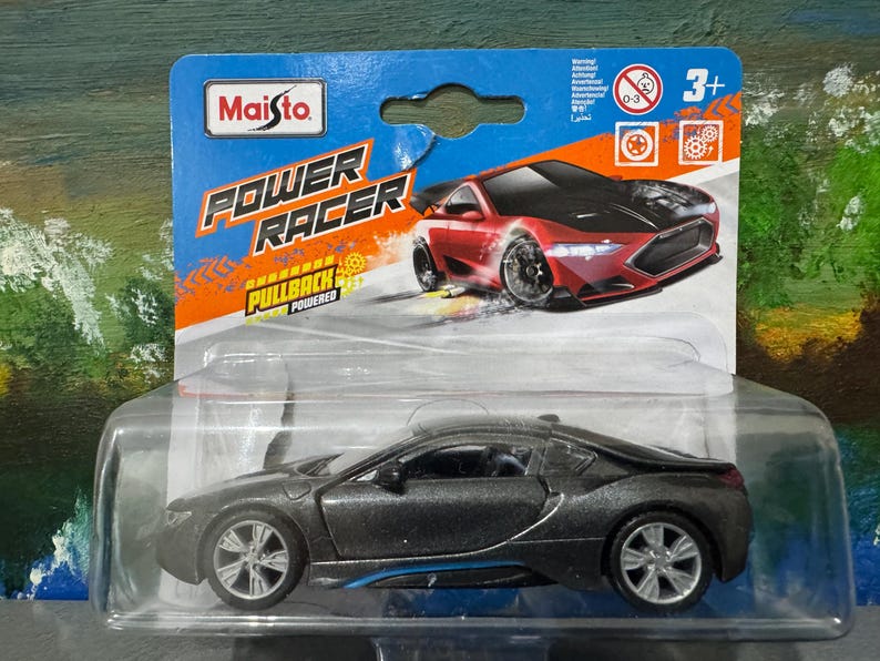 May include: A Maisto Power Racer toy car in a clear plastic package. The die-cast model is dark gray with blue accents. The packaging features a red sports car graphic and the text "POWER RACER".