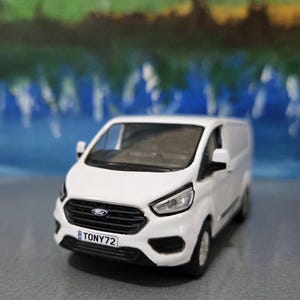 Puede incluir: Modelo de furgoneta Ford Transit blanca con parrilla y faros negros. El modelo tiene una matrícula que dice TONY72. La furgoneta es una réplica en miniatura de un vehículo comercial.
