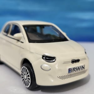 May include: A white toy car model of a Fiat 500 with a black number plate that reads "IRWIN".