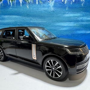 Puede incluir: Modelo de coche SUV Range Rover negro con un detalle de moldura plateada en el lateral. El coche está sobre una superficie blanca.